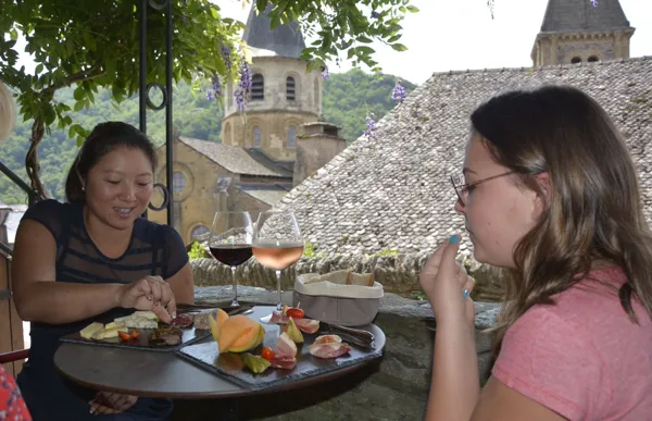 Profitez d'un moment à Conques pour aller boire une verre de vin et manger un plateau de charcuterie sous une terrasse ombragée